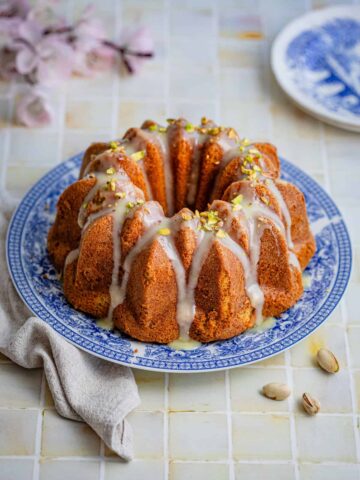bundt cake with white glaze and pistachios on a blue plate on a table