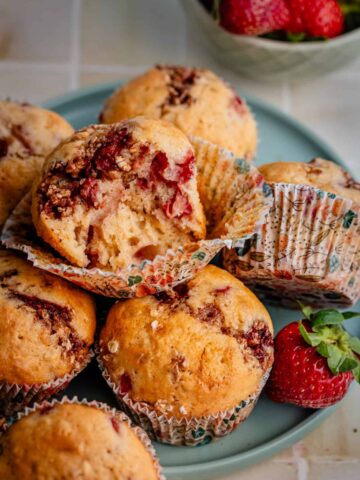 strawberry muffins on a plate, one half eaten, with the fruits aside
