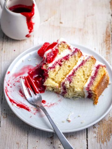 a slice of raspberry white chocolate cake with raspberry coulis aside