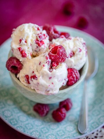 ice cream with raspberries in a bowl on a green plate on red tabletop
